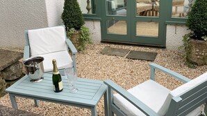En uteplats med ett bord, två stolar, en flaska champagne och ett glas.