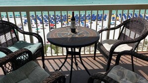 A balcony with wicker chairs and a table, overlooking a beach with umbrellas. - 8th Floor Pelican Beachfront with Ocean View (Destin)