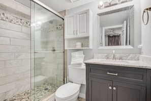A bathroom with a glass-enclosed shower, a white toilet, a vanity with dark cabinets, and a mirror above the sink.