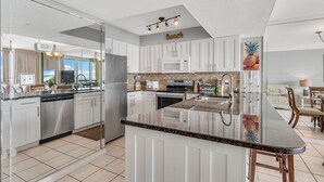 A modern kitchen with white cabinets, stainless steel appliances, and a granite countertop. - 8th Floor Pelican Beachfront with Ocean View (Destin)
