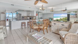 A spacious living area with a dining table, wicker furniture, and a large TV. - 8th Floor Pelican Beachfront with Ocean View (Destin)