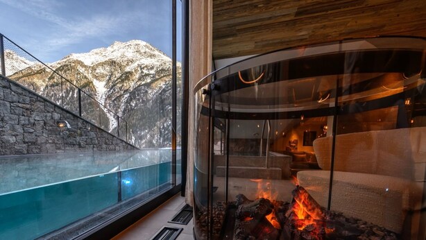 A modern interior with a glass fireplace, a stone wall, and a view of snow-capped mountains. - Appartement Mont Blanc by Interhome (Sölden)
