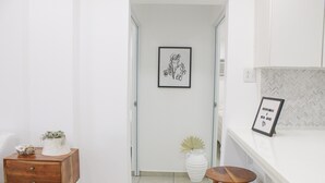 A hallway with a wooden nightstand, a white vase, and a framed picture on the wall.