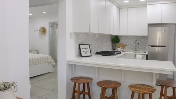 A modern kitchen with white cabinets, a stainless steel refrigerator, and a wooden bar stool seating area.