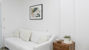 A white sofa with cushions, a small wooden side table with a plant, and a framed abstract artwork on the wall.