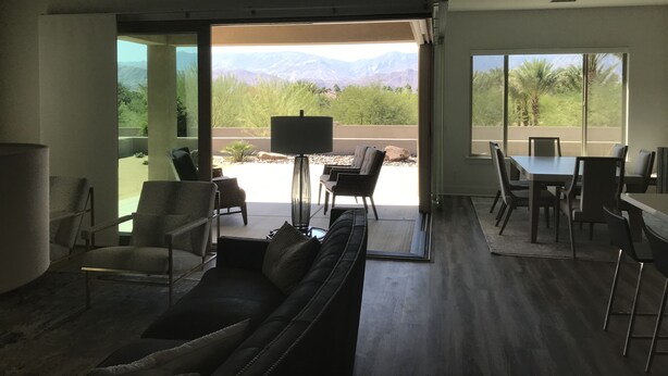 Un salon moderne comprenant un canapé, des fauteuils, une table basse et un coin repas avec une table et des chaises. De grandes fenêtres offrent une vue sur les montagnes et la verdure.