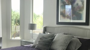 Une chambre à coucher avec un lit, des oreillers, une lampe et un tableau accroché au mur.