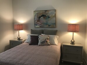 Une chambre à coucher comprenant un lit, deux tables de chevet, deux lampes et un tableau abstrait accroché au mur.