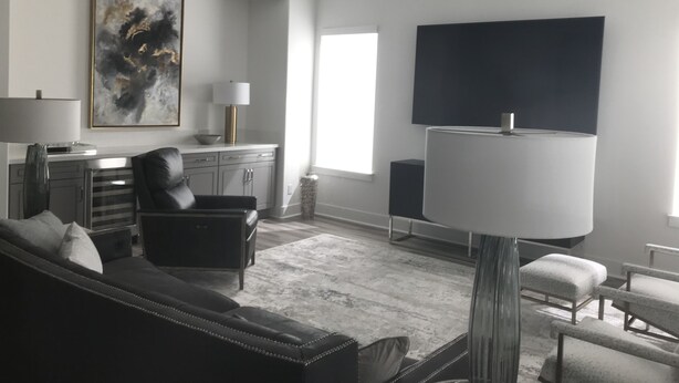 Ein modernes Wohnzimmer mit einer schwarzen Ledersofa, einem Couchtisch, einem an der Wand montierten Fernseher und einem großen abstrakten Gemälde.