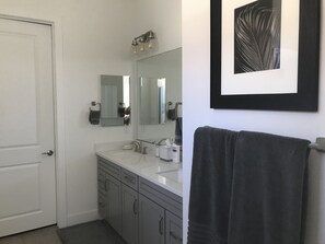 Une salle de bain moderne avec un lavabo blanc, un grand miroir et une œuvre d’art encadrée au-dessus du lavabo.