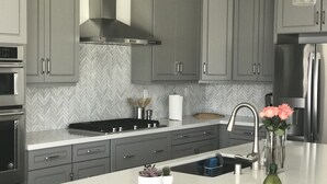 Une cuisine moderne avec des meubles gris, une hotte en acier inoxydable, un four encastré et un plan de travail blanc.