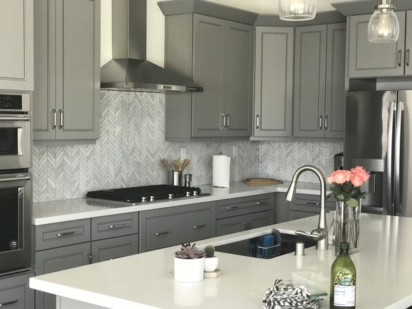 Une cuisine moderne avec des meubles gris, une hotte en acier inoxydable, un four encastré et un plan de travail blanc.