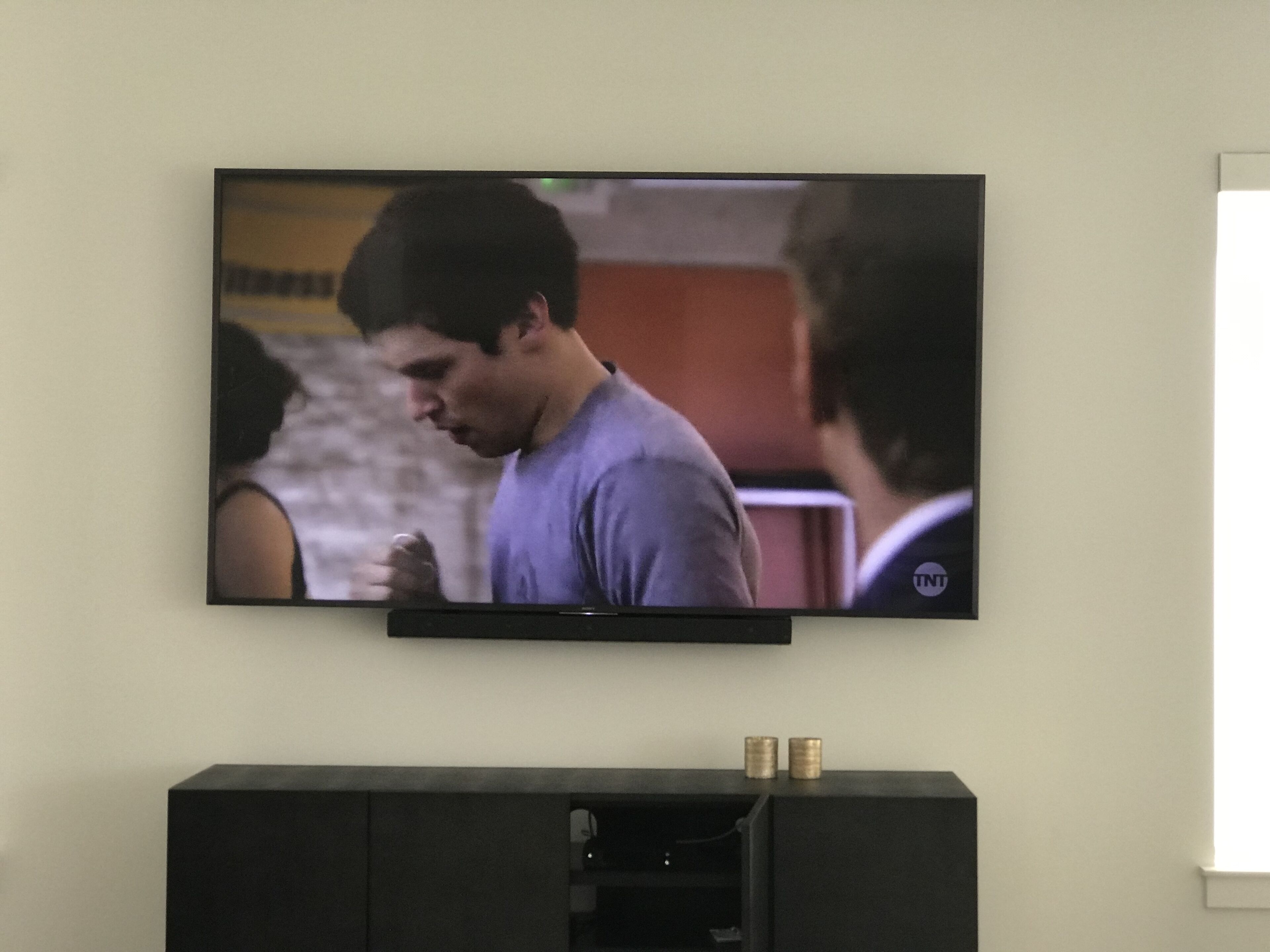 Un téléviseur à écran plat fixé au mur, au-dessus d’un meuble en bois foncé.