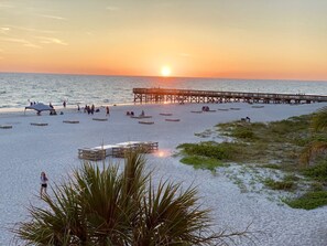 Una spiaggia con un molo che si protende nell'acqua, alcune persone e un tramonto.