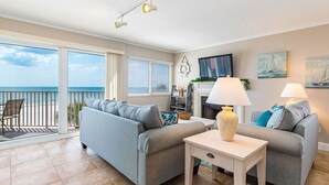 Ein Wohnzimmer mit zwei grauen Sofas, einem kleinen Tisch, einem Fernseher und einem Balkon mit Meerblick.