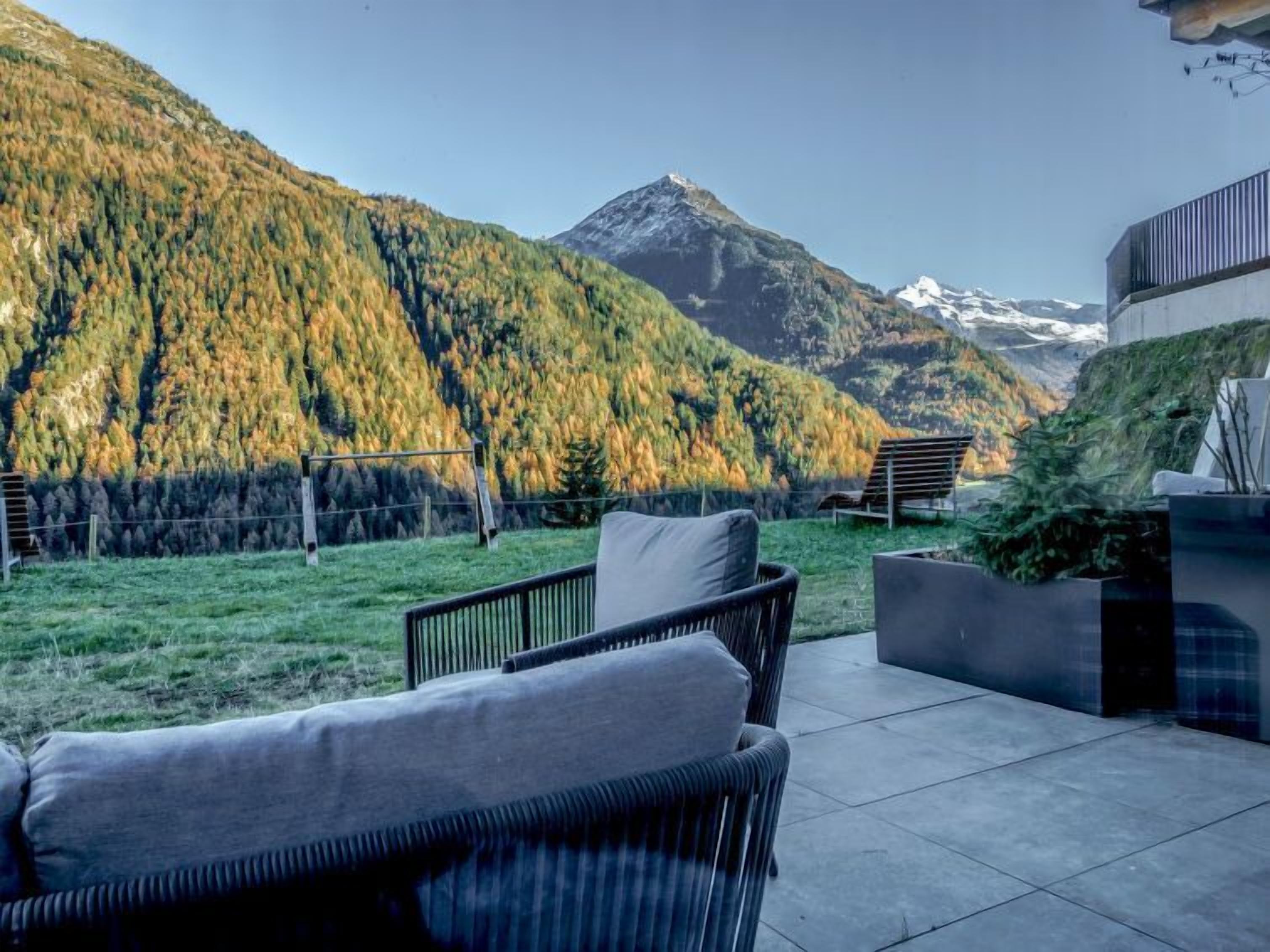 A patio with outdoor furniture, a view of a mountain, and a building with a green roof.