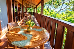 A wooden deck with a round table and chairs, surrounded by a wooden railing, overlooking a lush green landscape. - Rohotu Fare (Bora Bora)