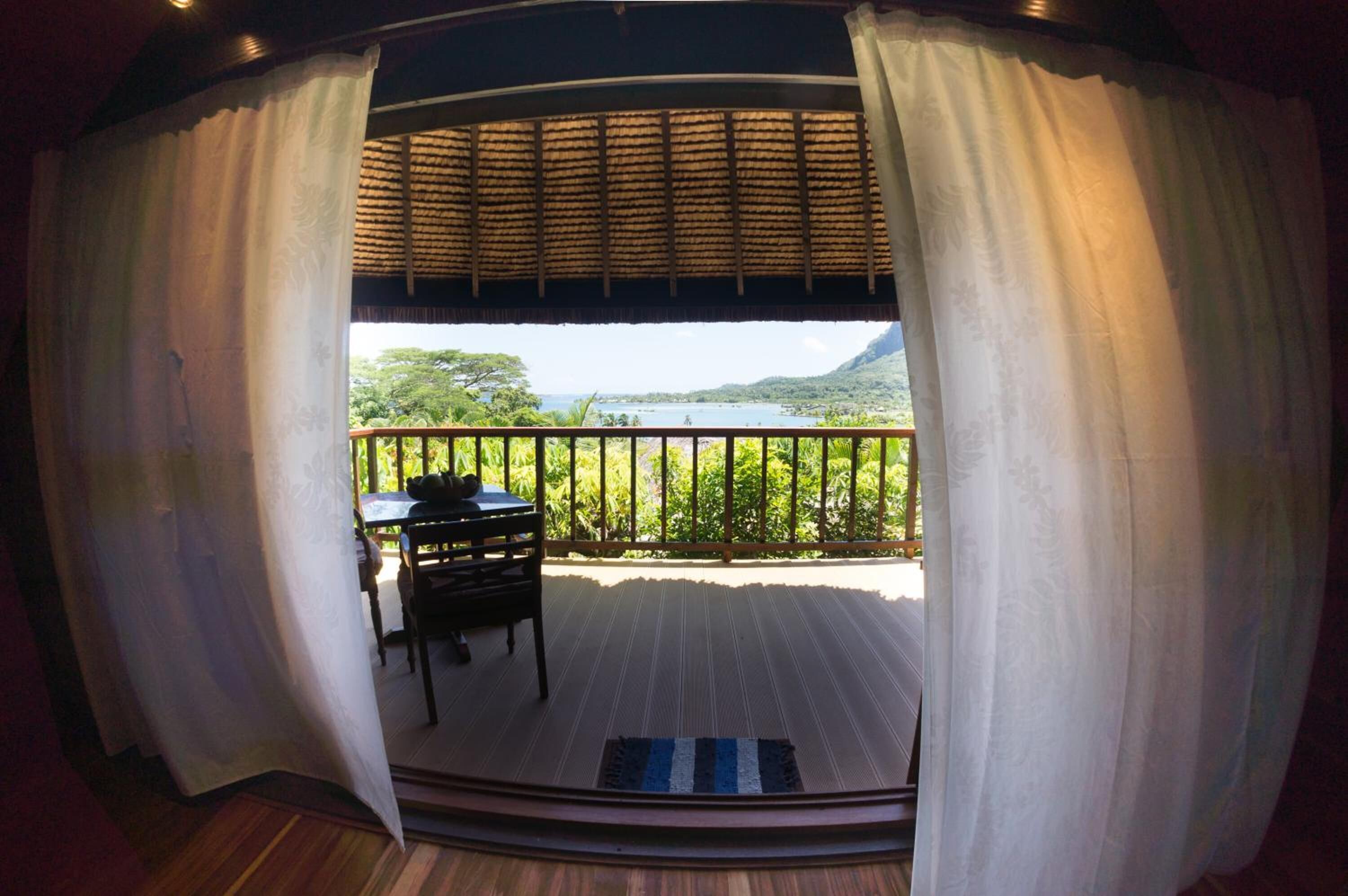 A room with a view of a lake and mountains. There is a table and a chair in the room.