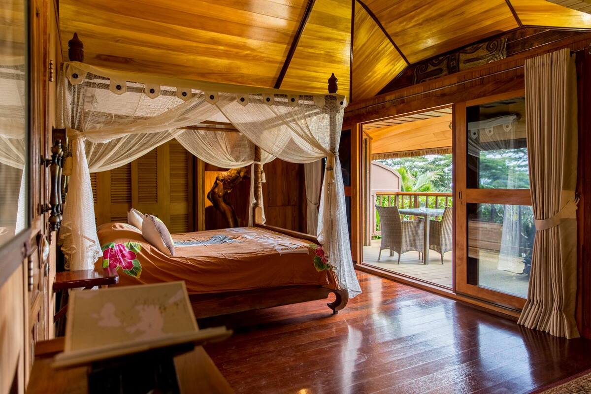 A bedroom with a canopy bed, wooden flooring, and a view of the outdoors.