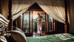 A room with a bed, a window with curtains, and a view of greenery outside.