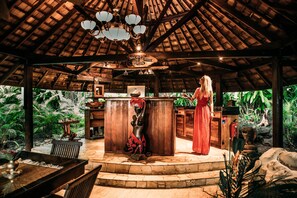 Une structure en bois avec un toit de chaume, un bar central et des plantes tropicales tout autour.