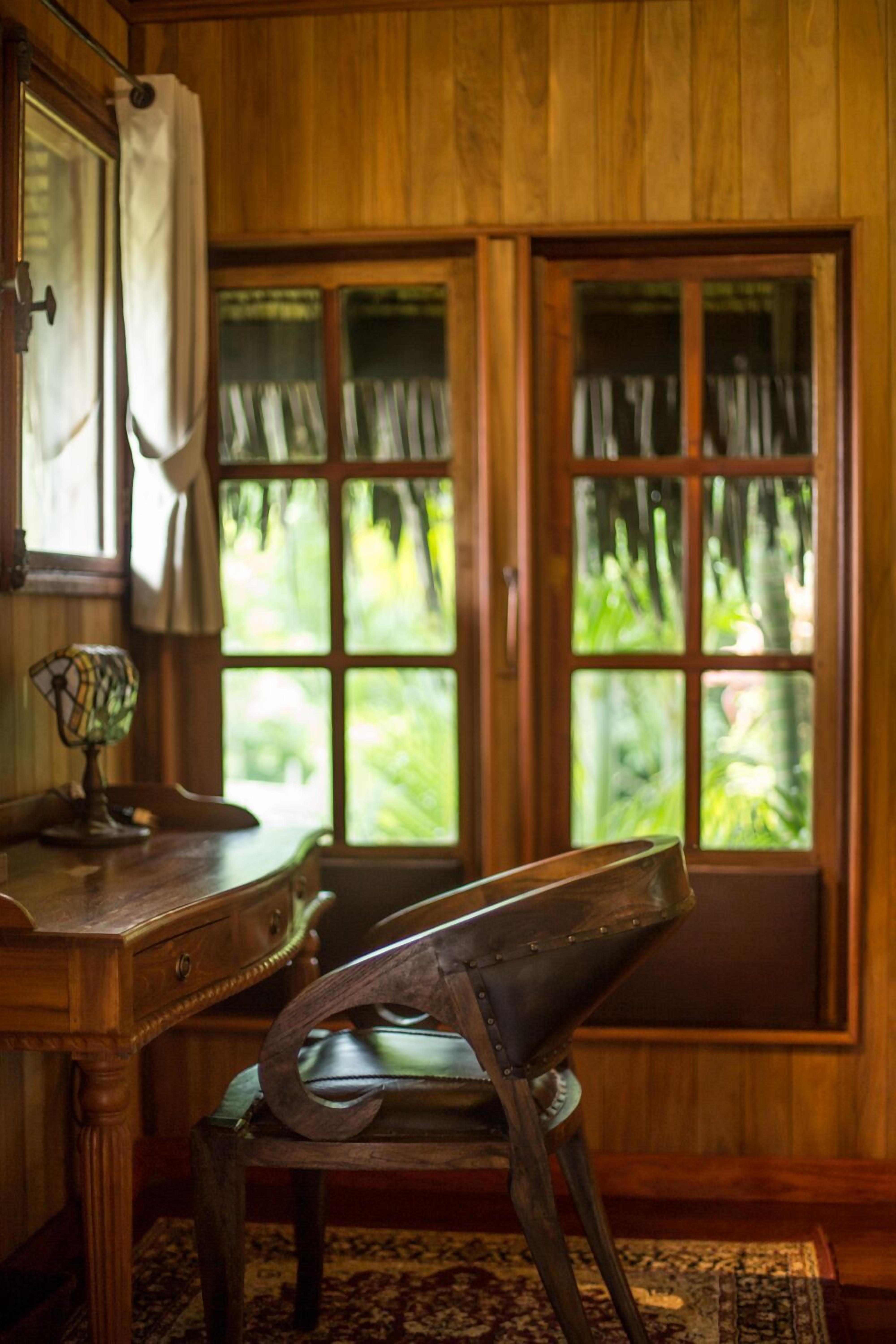 Een kamer met houten vloer, een bureau, een stoel en een raam met gordijnen.