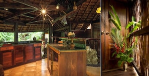 Un interior de madera con una isla central, armarios de madera y una planta grande cerca de la puerta.