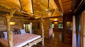 A spacious bedroom with a large bed, wooden ceiling beams, and a ceiling fan. - Rohotu Fare (Bora Bora)