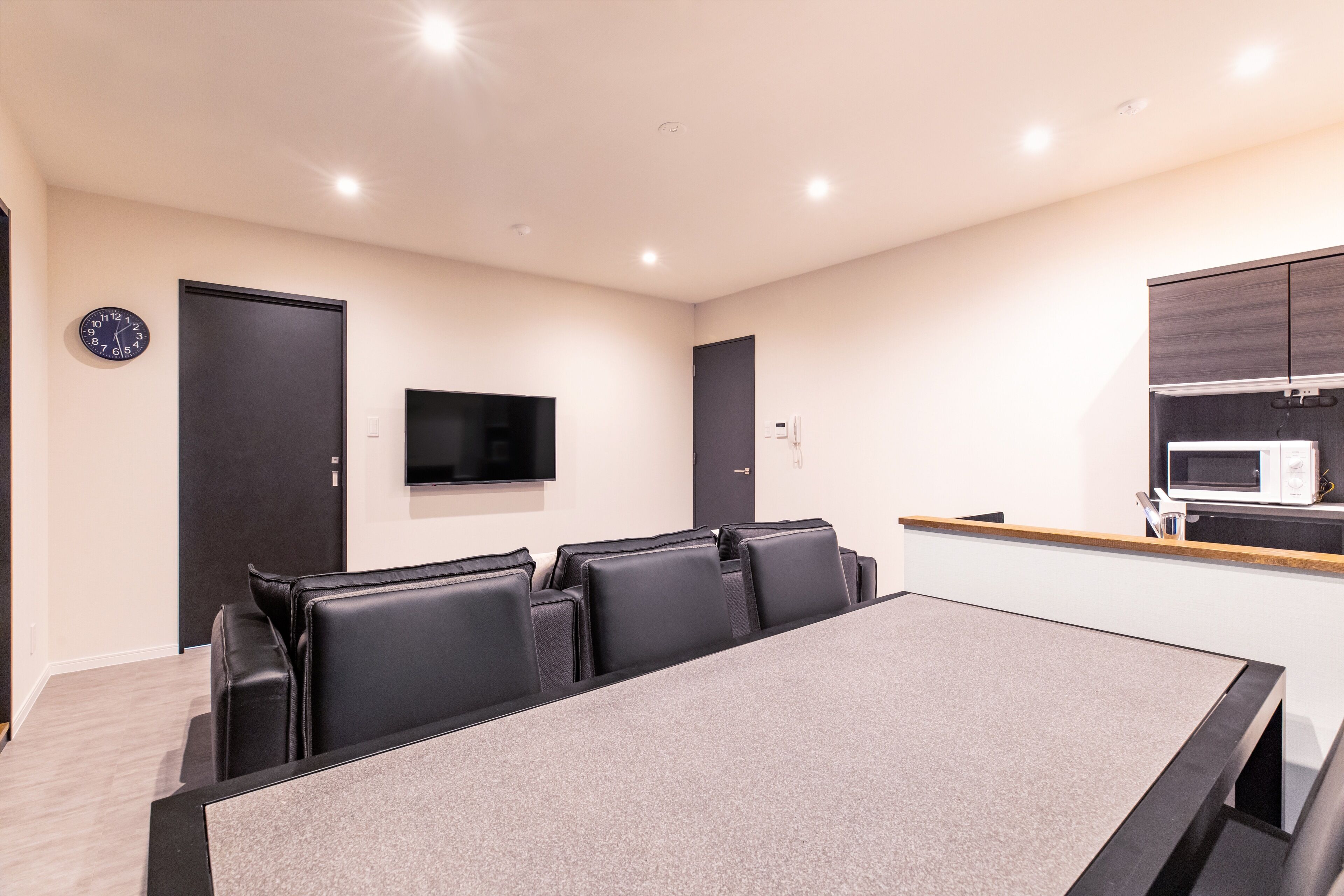 A conference room with a long table and black chairs, a flat-screen TV on the wall, and a microwave in the kitchenette area.