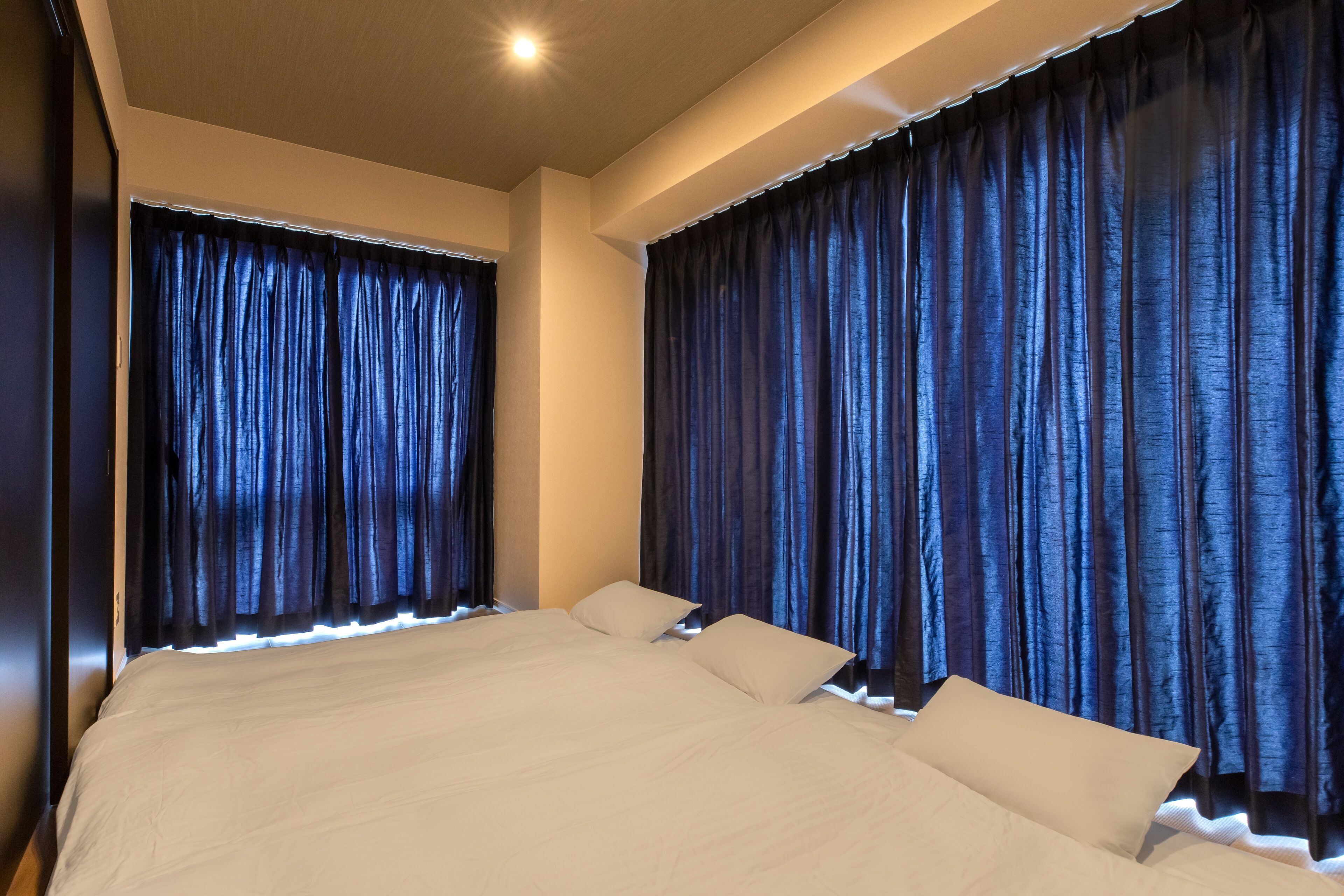 Uma cama grande com lençóis brancos e duas almofadas, com cortinas escuras de cada lado.