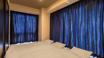 Uma cama grande com lençóis brancos e duas almofadas, com cortinas escuras de cada lado.