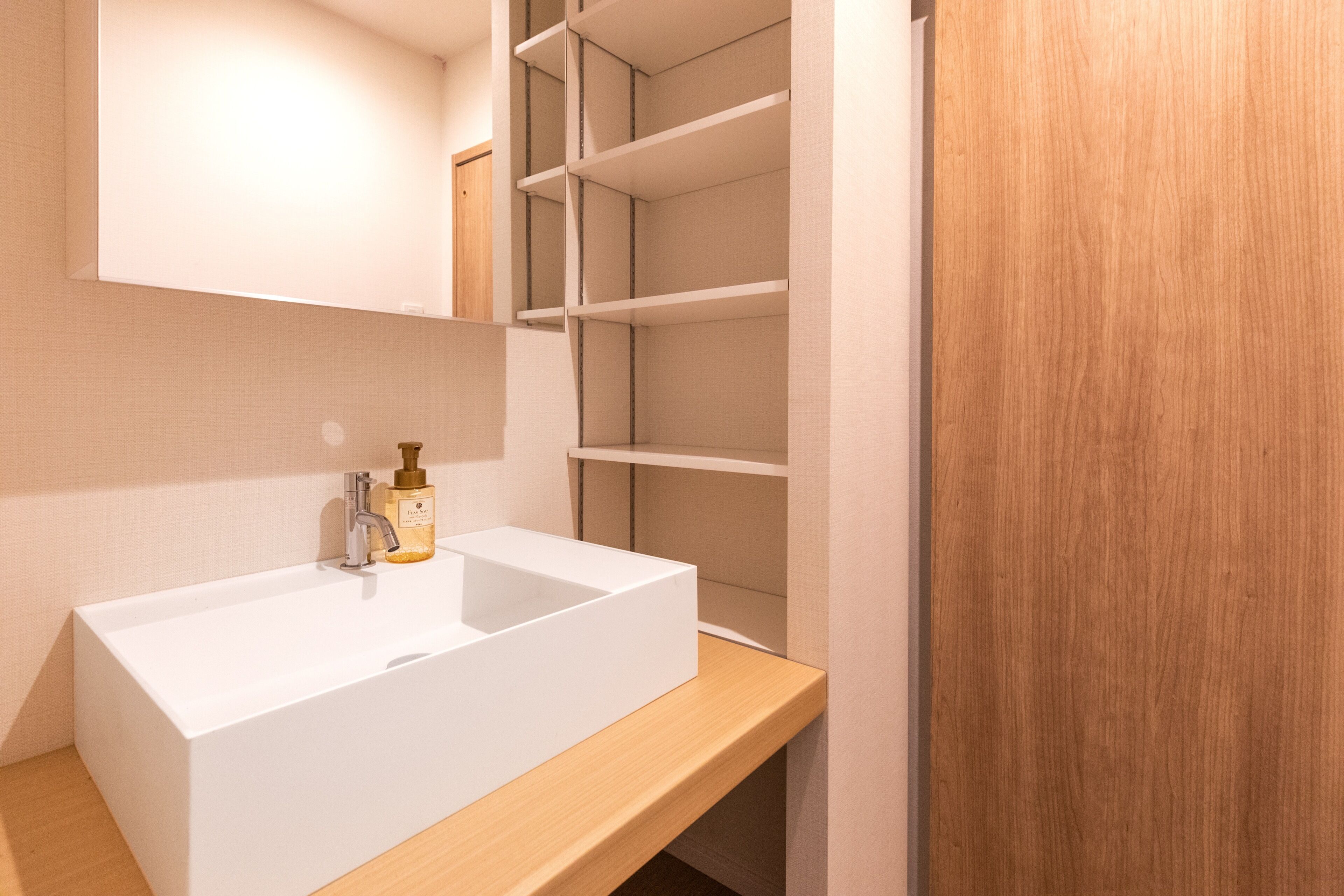 A modern bathroom with a white sink, wooden vanity, and built-in shelving.