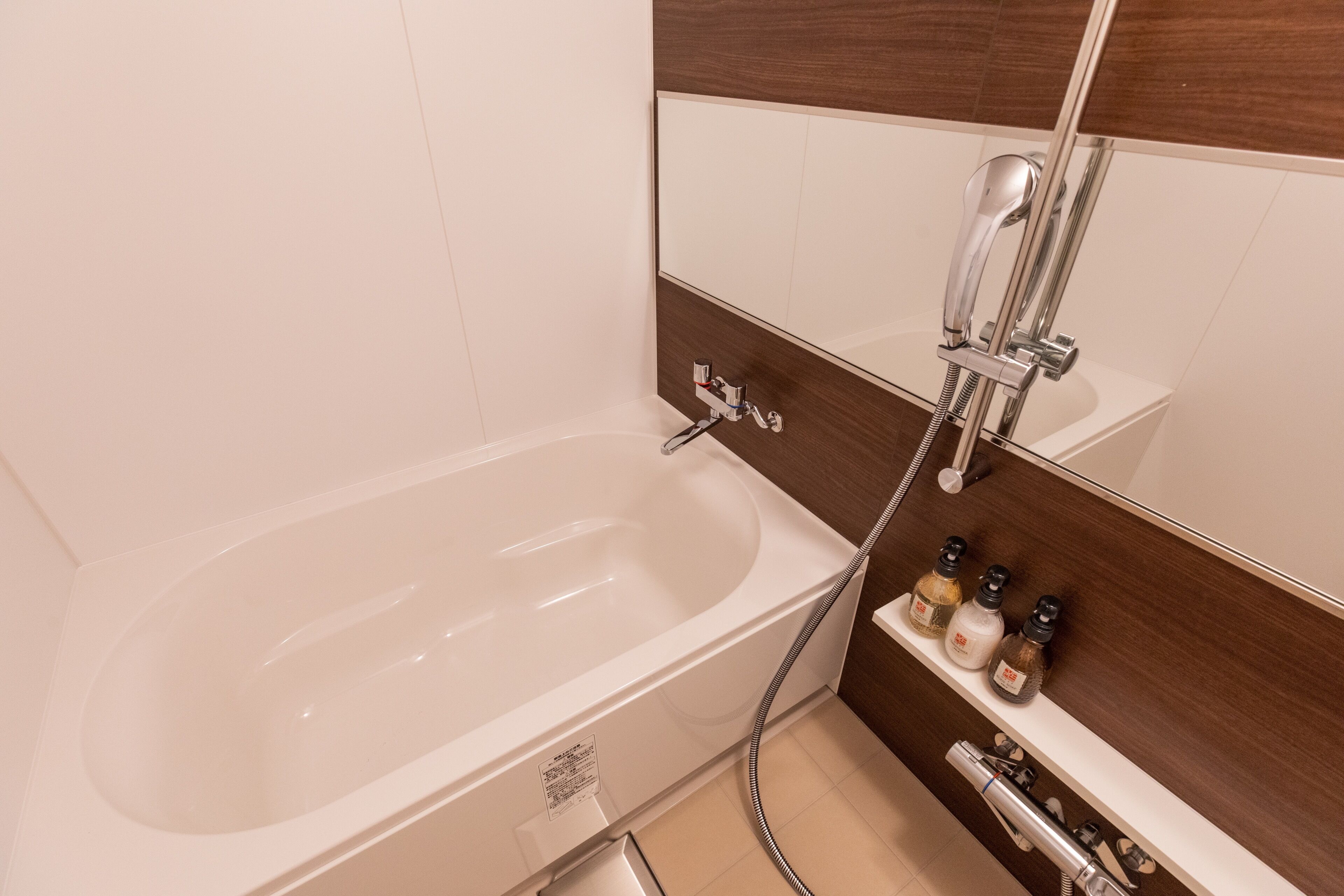 A modern bathroom with a freestanding bathtub, a handheld showerhead, and a shelf with toiletries.