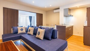 A modern living room with a sofa, a small wooden table, and a kitchen area with a sink and cabinets.