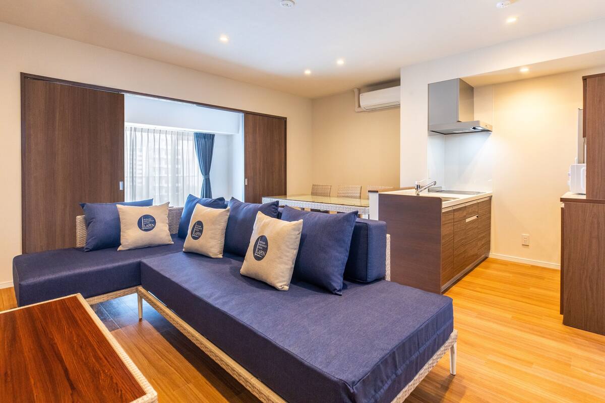 Uma sala de estar moderna com um sofá, uma pequena mesa de madeira e uma área de cozinha com pia e armários.