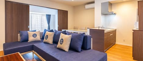Ein modernes Wohnzimmer mit einer Couch, einem kleinen Holztisch und einer Küchenzeile mit Spüle und Schränken.