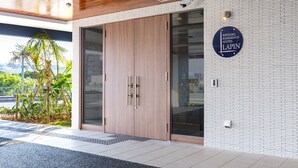 A modern hotel entrance with a large wooden door, a glass wall, and a sign indicating the hotel name.
