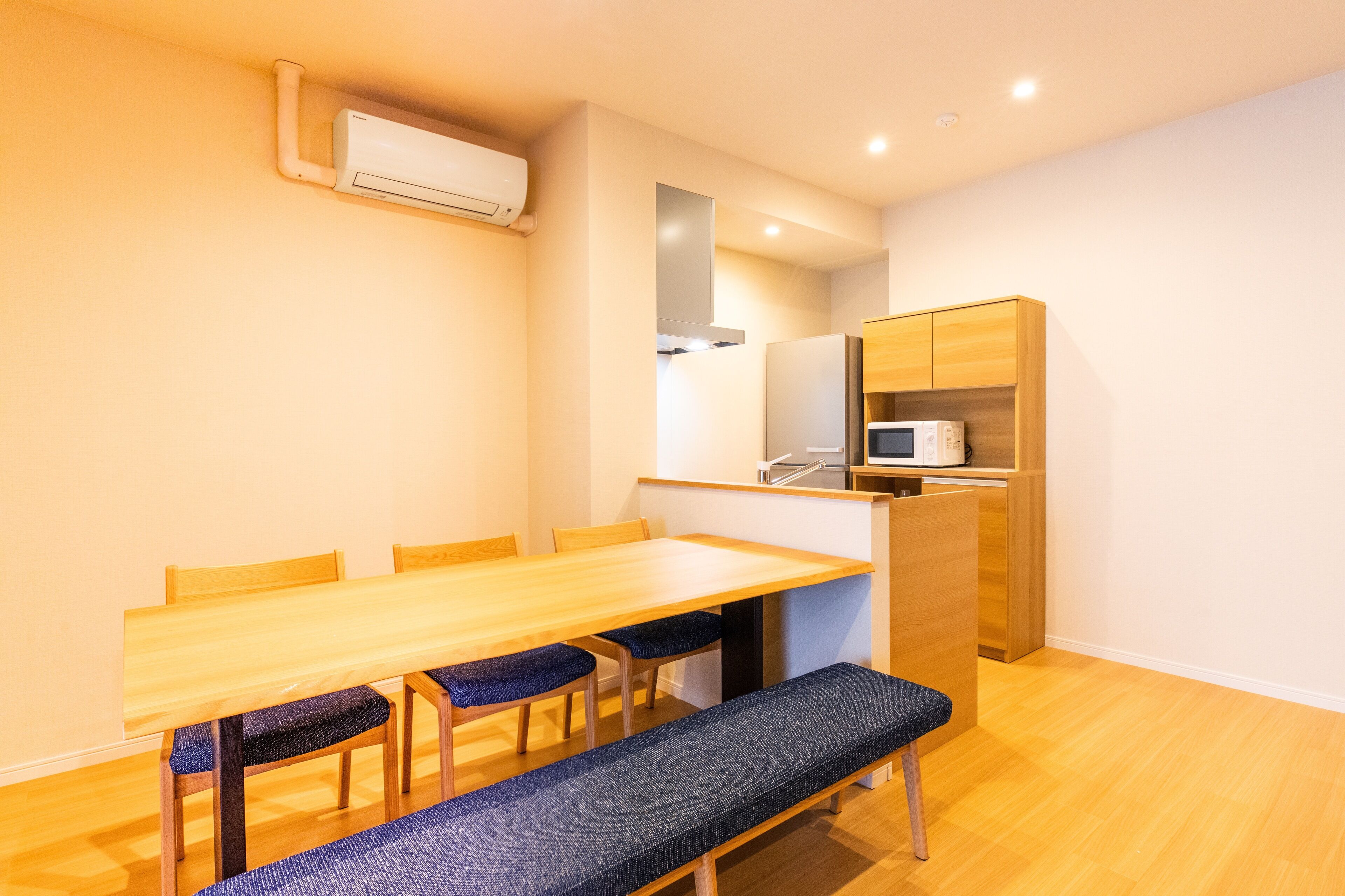 A compact kitchen with a wooden table, chairs, a bench, and a microwave.