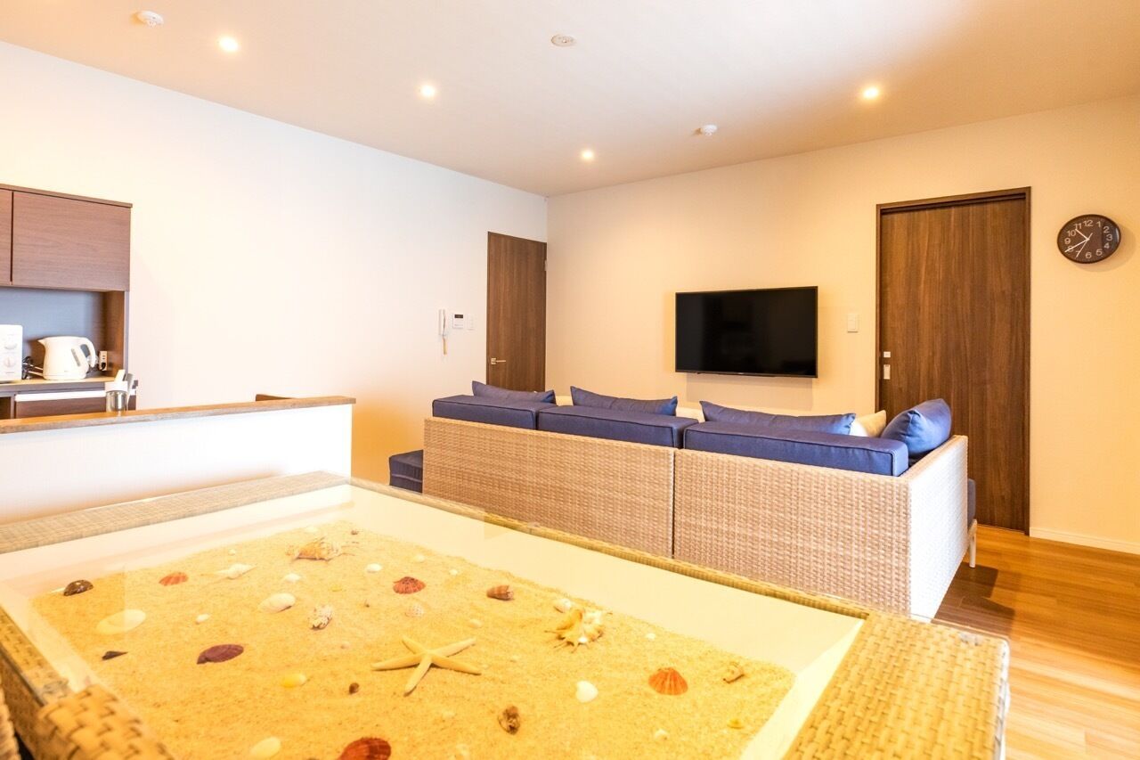 A modern living room with a large TV, a sofa with blue cushions, and a coffee machine.