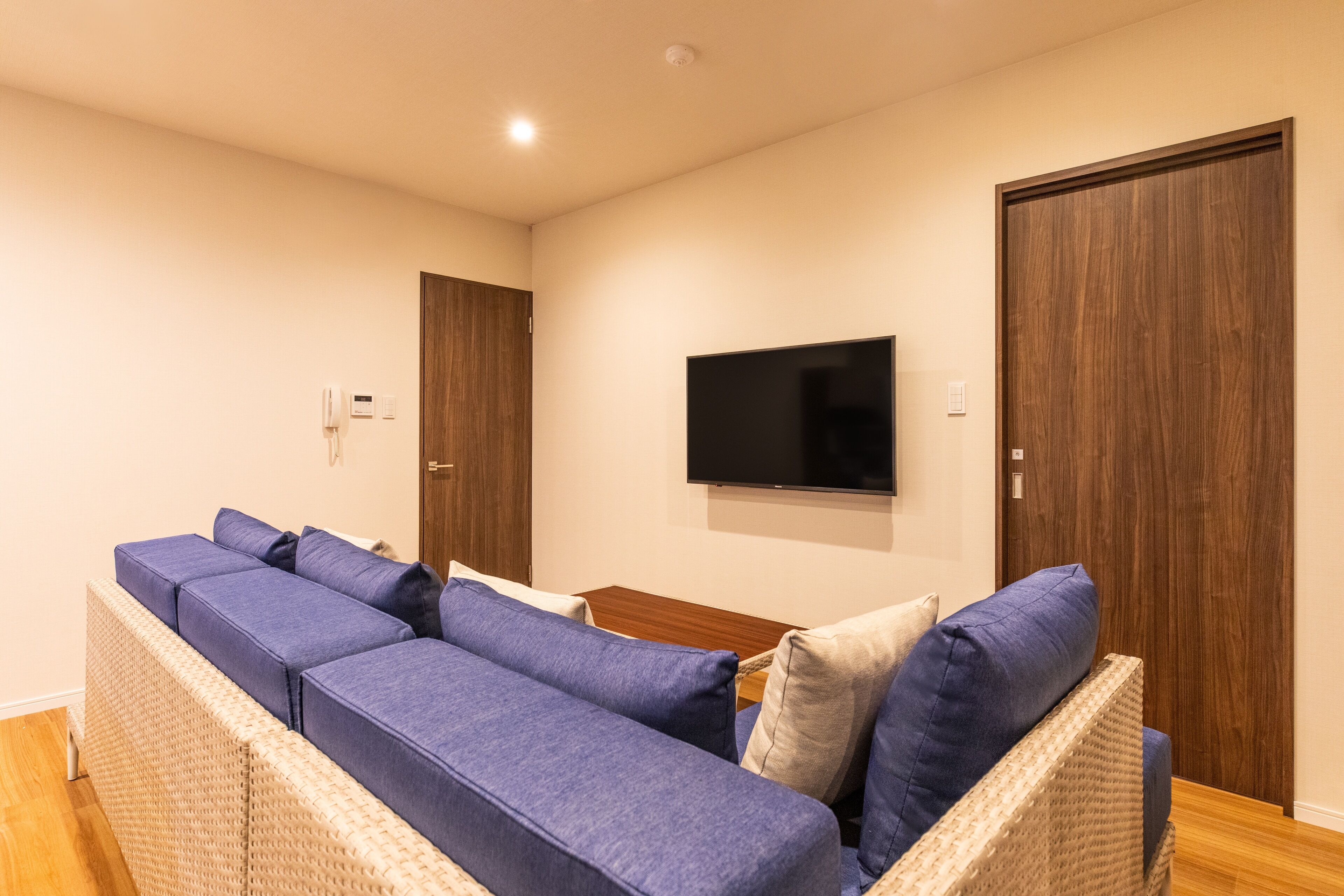 A modern living room with a large sectional sofa, a flat-screen TV mounted on the wall, and wooden doors.