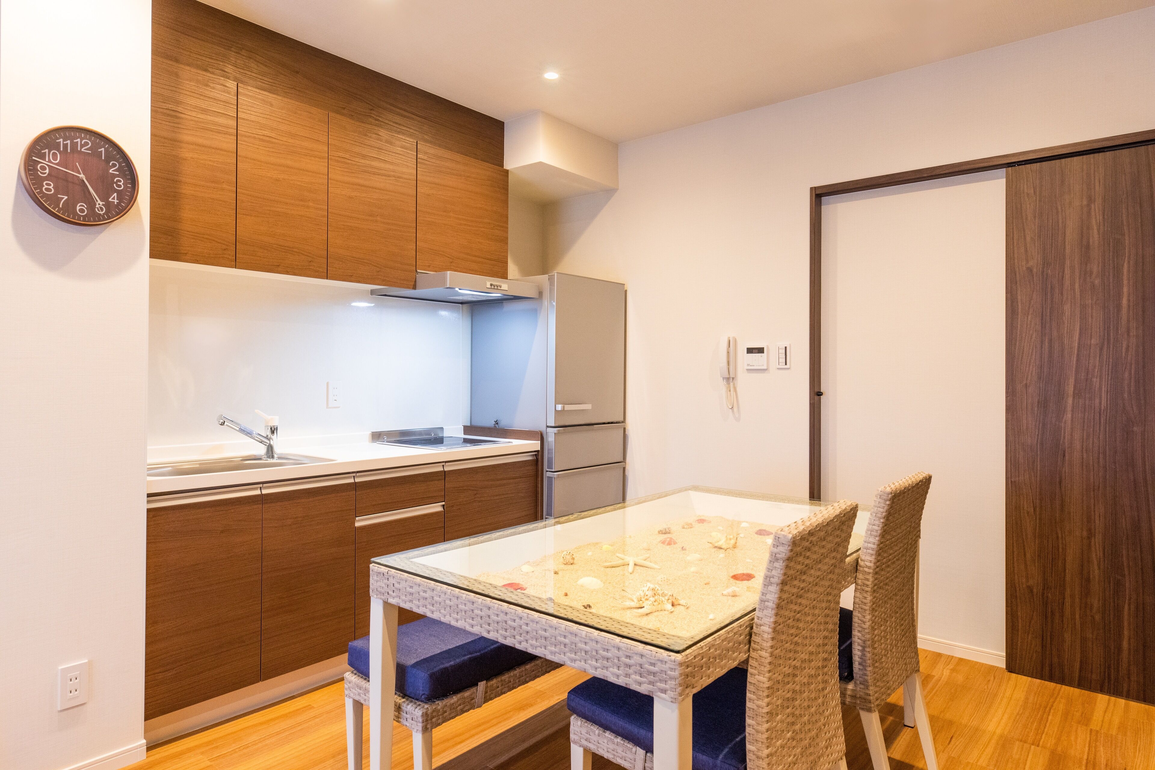 Une cuisine moderne avec des meubles en bois, un évier en acier inoxydable et une table à manger en verre, accompagnée de chaises en osier.