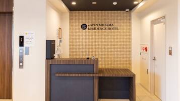 Mostrador de recepción en el Lapin Mihama Residence Hotel, con un muro de azulejos, una puerta de madera y un ascensor.