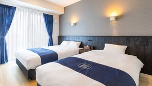 A hotel room with two beds, a large window with curtains, a wall-mounted light, and a wooden headboard.