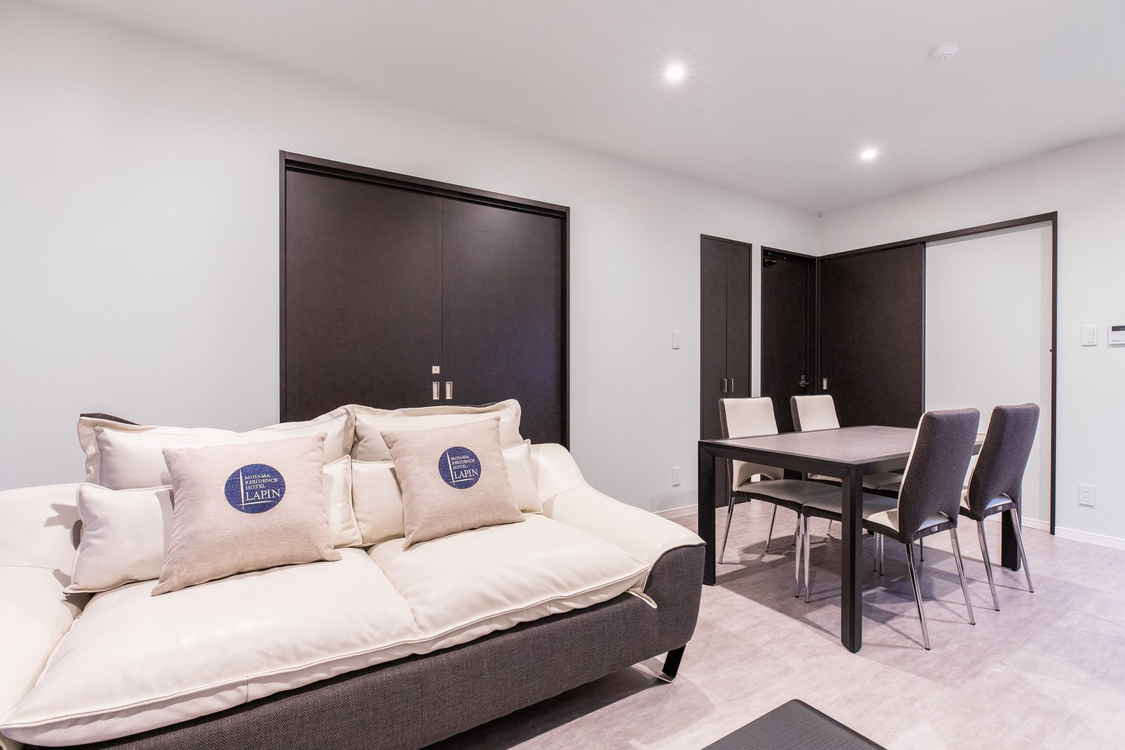 A modern hotel room with a sofa, a dining table, and chairs.