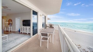 Ein Balkon mit Tisch und Stühlen, einem Fernseher und Blick auf das Meer.