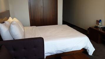 Hotellihuone, jossa on sänky, puinen pääty, yöpöytä lampun kanssa ja työpöytä tuolilla.