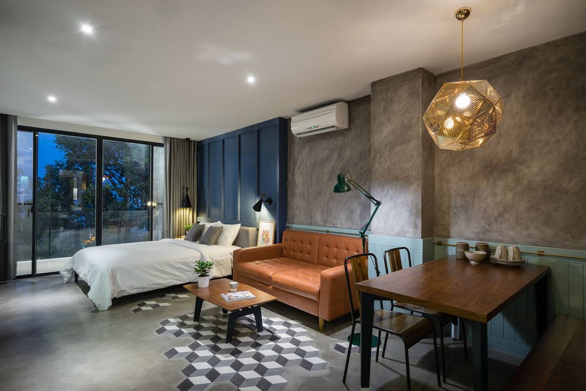 Ein modernes Hotelzimmer mit Bett, Sofa, Esstisch und einem großen Fenster.