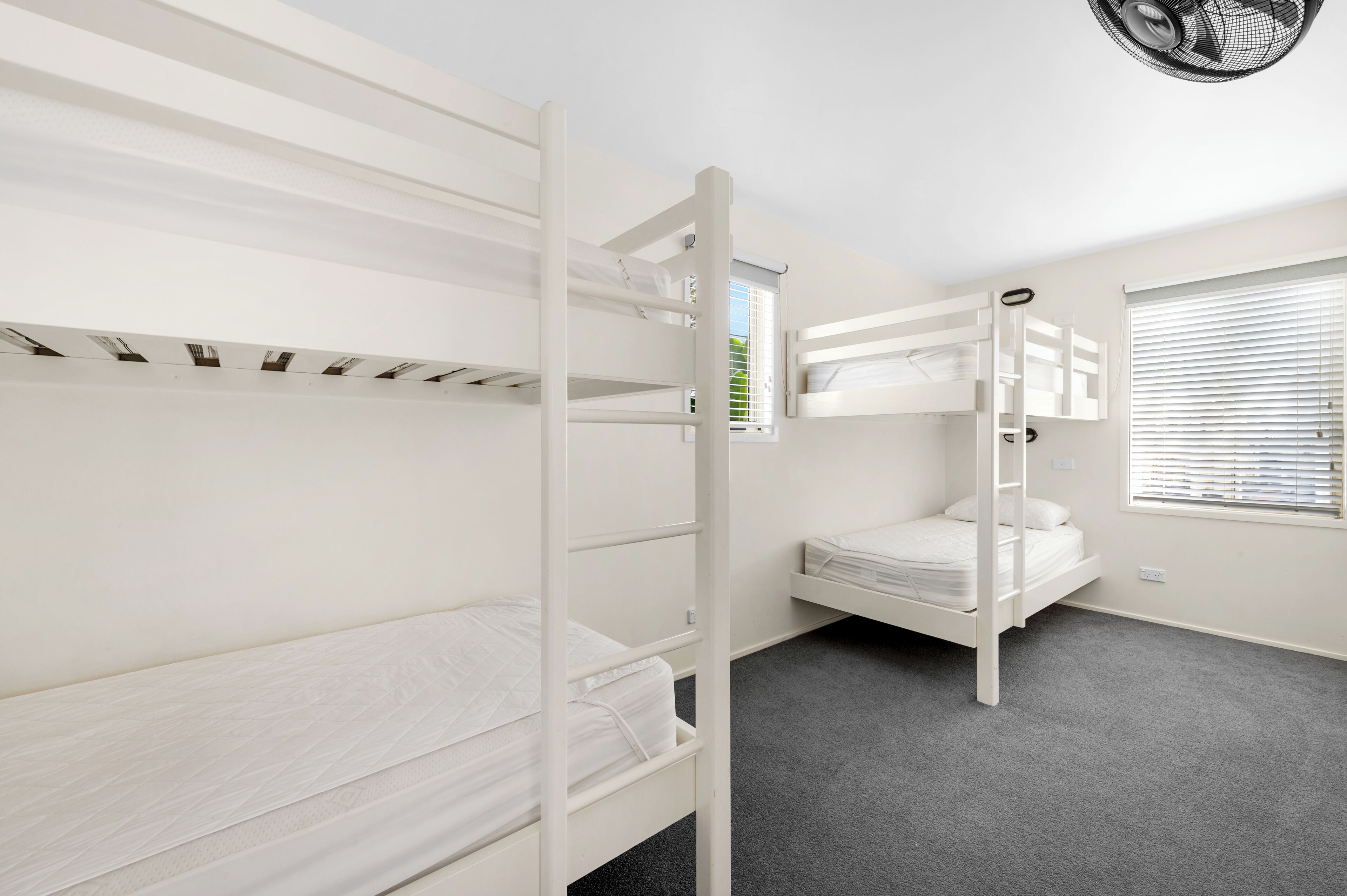 A bunk bed room with a grey carpet, white walls, and a window with blinds.