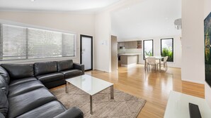 A modern living room with a sectional sofa, a glass coffee table, and a dining area with a table and chairs. - Mountain View Resort (Shoalhaven Heads)