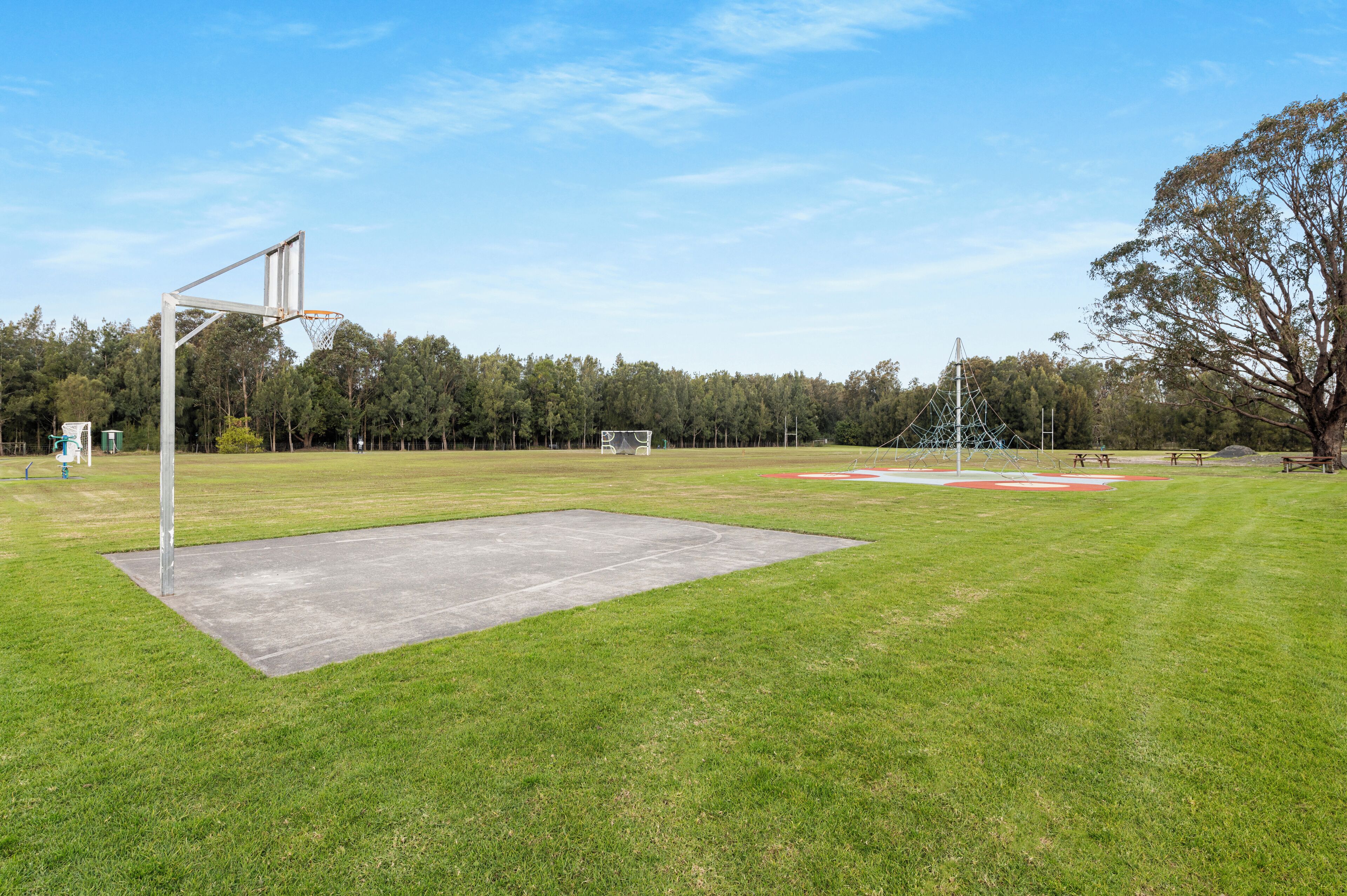 An outdoor basketball court with a hoop, a concrete area, and a baseball diamond in the background.